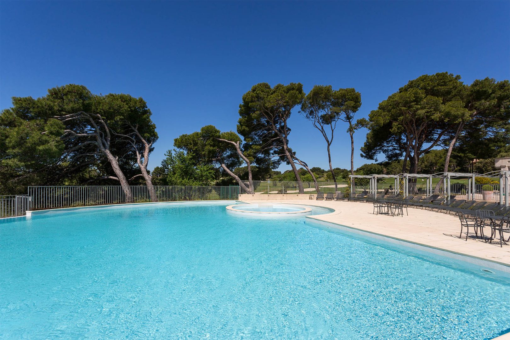 Image de la résidence Provence Country Club de Madame Vacances : piscine extérieure entourée de pins, avec des transats et une terrasse sous un ciel bleu dégagé